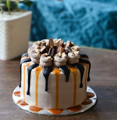 A chocolate cake with a caramel drizzle and chocolate pieces on top